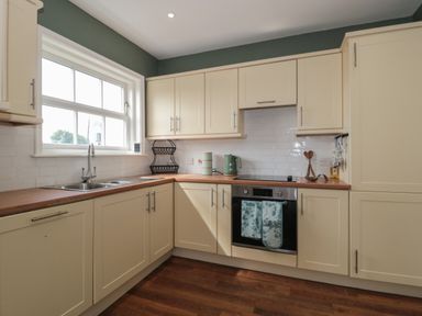 A kitchen with cream cabinets wooden countertops a window stainless steel sink oven and kitchen utensils at Cherry Tree House in Highbridge