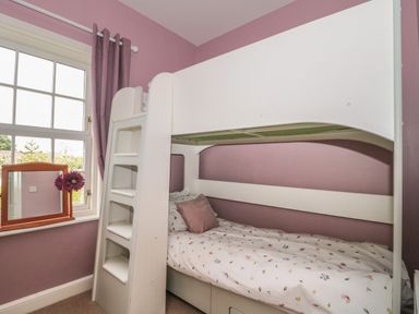 A bedroom with a white bunk bed beside a window with purple curtains at Cherry Tree House in Highbridge
