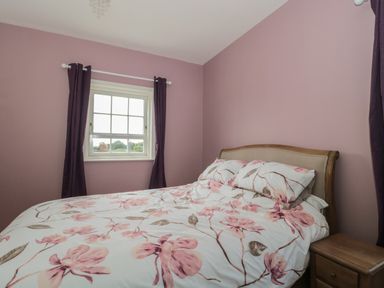 A bedroom with a bed covered in floral bedding next to a wooden nightstand and a window with dark curtains at Cherry Tree House in Highbridge
