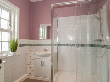 A bathroom with a shower enclosure a sink cabinet and a window with a plant at Cherry Tree House in Highbridge