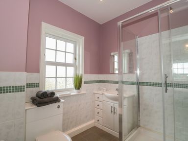 A bathroom with a shower enclosure, sink with cabinet, toilet, a window with frosted glass, towels on the toilet tank, and a plant on the window sill at Cherry Tree House in Highbridge