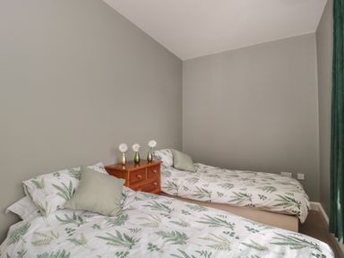 A bedroom with two single beds a wooden bedside table with three vases and green curtains at Cherry Tree House in Highbridge