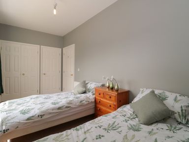 A bedroom with two single beds a wooden dresser and closed white doors at Cherry Tree House in Highbridge