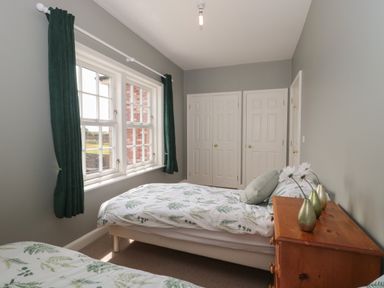 A bedroom with two single beds green curtains and a wooden chest of drawers at Cherry Tree House in Highbridge