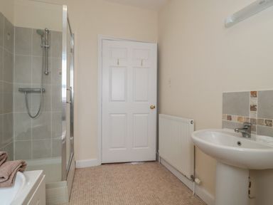 A bathroom with a shower, sink, radiator, and a white door at Cherry Tree House in Highbridge