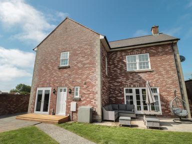 A brick house with a small wooden deck patio furniture and a hanging chair in the garden at Cherry Tree House in Highbridge