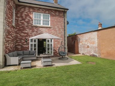 An outdoor patio area with a grey cushioned sofa set umbrella and hanging chair next to a brick house at Cherry Tree House in Highbridge