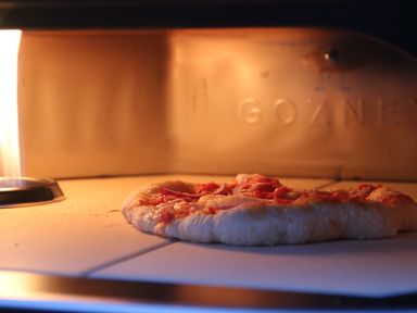 A pizza baking inside a pizza oven with flames visible on the left at Cherry Tree House in Highbridge
