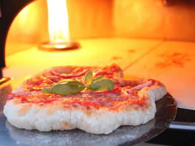 A pizza baking inside a pizza oven with a flame visible at the back