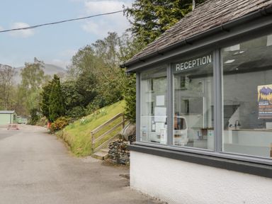 A reception building next to a road with trees and hills in the background at Beech Timber Lodge in Keswick