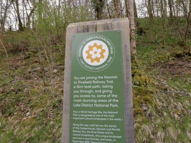 A wooden signpost with information about the Keswick to Threlkeld Railway Trail in a wooded area at Beech Timber Lodge in Keswick