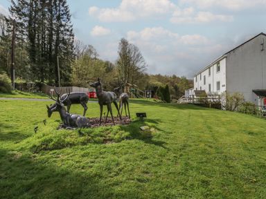 A grassy outdoor area with statues of four deer and a white building in the background at Elm Lodge in Keswick