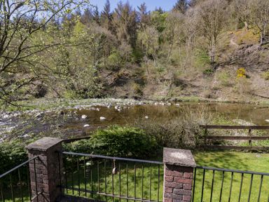 A garden view with a river and trees at Elm Lodge in Keswick