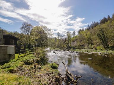 A river surrounded by trees and a cabin at Elm Lodge in Keswick