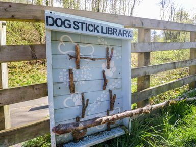 A dog stick library with wooden sticks mounted on a sign near a fence in a park