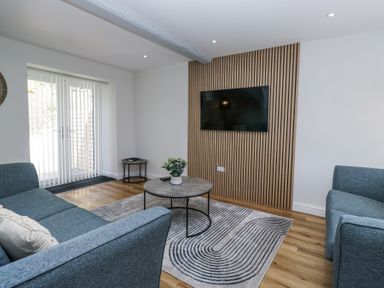 A sitting room with two blue sofas a round coffee table a wall-mounted TV and sliding glass doors at Riverside Cottage No 3 in Keswick