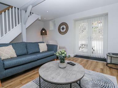 A living room with a blue sofa a round coffee table with a plant a wall clock and glass doors with vertical blinds at Riverside Cottage No 3 Keswick