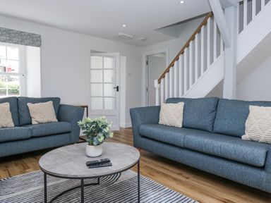 A living room with two blue sofas a round coffee table with a plant and remote controls and a staircase in Riverside Cottage No 3 in Keswick