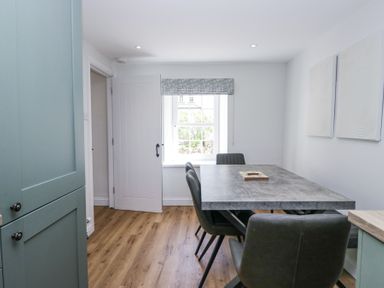 A dining area with a rectangular table and six chairs next to a window with a patterned blind at Riverside Cottage No 3 in Keswick