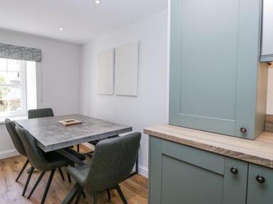 A dining area with a rectangular table and six chairs next to green kitchen cabinets at Riverside Cottage No 3 in Keswick
