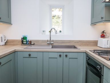 A kitchen with a sink under a window flanked by cabinets a kettle a toaster and a fire extinguisher at Riverside Cottage No 3 in Keswick