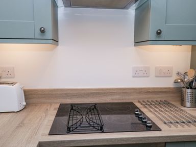 A kitchen countertop with an electric hob, a white toaster, and utensils in a holder at Riverside Cottage No 3 in Keswick