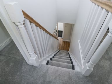 A carpeted staircase with white banisters and wooden handrail leading down to a hallway with wooden floor at Riverside Cottage No 3 Keswick