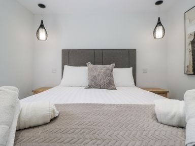 A bedroom with a double bed white pillows a patterned cushion bedside tables pendant lights and folded towels at Riverside Cottage No 3 in Keswick