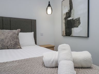 A bedroom with a bed pillow bedside table hanging light and abstract wall art at Riverside Cottage No 3 Keswick