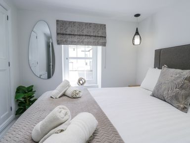 A bedroom with a bed towels on it a window with a blind and an oval mirror on the wall at Riverside Cottage No 3 in Keswick