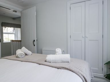 A bedroom with a made bed topped with folded white towels next to a closed white closet and an open door showing a window at Riverside Cottage No 3 in Keswick