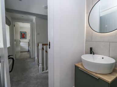 A hallway with a staircase and a bathroom with a sink and round mirror at Riverside Cottage No 3 in Keswick