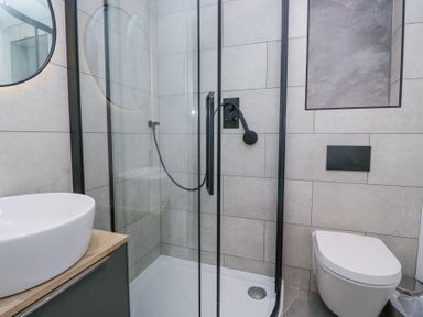 A bathroom with a glass shower enclosure a white sink on a wooden countertop and a wall-mounted toilet at Riverside Cottage No 3 Keswick