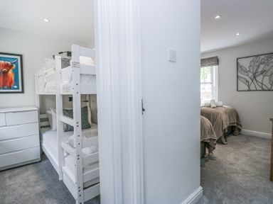A hallway showing a bedroom with white bunk beds and dresser on the left and a bedroom with two single beds on the right at Riverside Cottage No 3 in Keswick