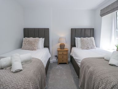 A bedroom with two single beds a wooden nightstand with a lamp between the beds and a window at Riverside Cottage No 3 in Keswick