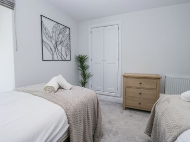 A bedroom with two beds a wooden chest of drawers a built in cupboard and a plant at Riverside Cottage No 3 in Keswick