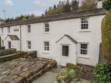 An exterior view of a white cottage with a stone roof and multiple windows at Riverside Cottage No 5 in Keswick