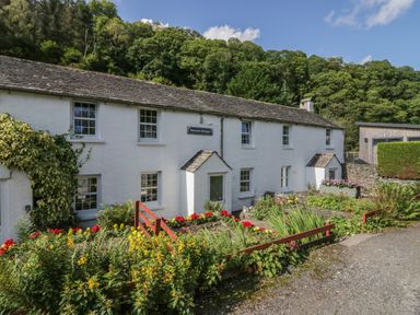 A white cottage with flower beds and a gravel path at Riverside Cottage No 5 in Keswick