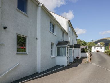 A driveway next to a white building with windows and small porch entrances at Garden Cottage No 1 in Keswick