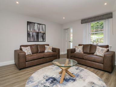 A living room with two brown sofas a round glass coffee table and a circular rug at Garden Cottage No 1 in Keswick