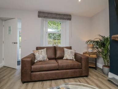 A brown sofa with two patterned cushions in a living room with wooden flooring and a side table with a lamp and plant at Garden Cottage No 1 in Keswick