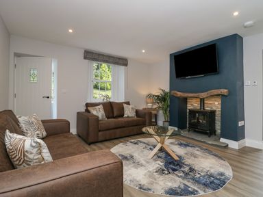 A living room with brown sofas a round rug and a television above a fireplace at Garden Cottage No 1 in Keswick