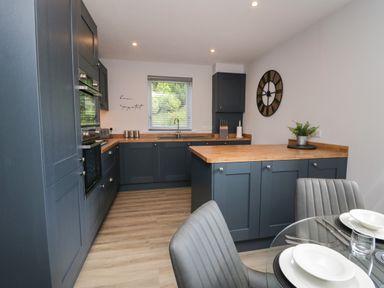 A kitchen with blue cabinets wooden countertops a dining table set with white plates and grey chairs at Garden Cottage No 1 in Keswick