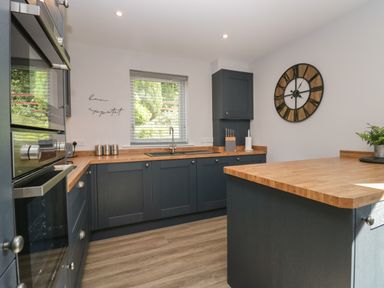 A kitchen with wooden countertops blue cabinets a wall clock and a window at Garden Cottage No 1 in Keswick