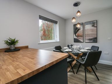 A dining area with a round glass table set for six and a wooden countertop with a plant at Garden Cottage No 1 in Keswick