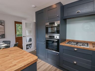 A kitchen with dark cabinets a gas stove two built-in ovens wooden countertops and a dining area at Garden Cottage No 1 in Keswick