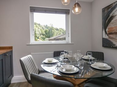 A dining area with a round glass table set for four near a window with a view of trees at Garden Cottage No 1 in Keswick