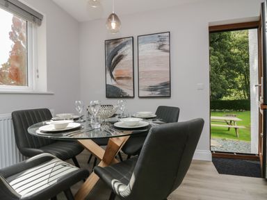 A dining area with a glass table set with dishes and four black chairs by an open door to a garden at Garden Cottage No 1 in Keswick