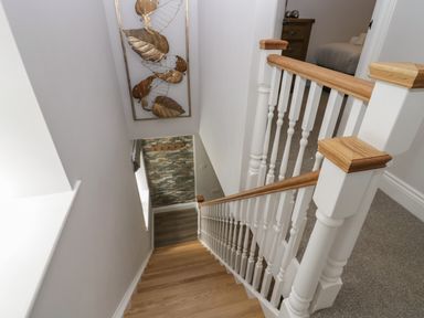 A stairway with wooden steps and white balusters leading down from a carpeted upper floor at Garden Cottage No 1 in Keswick