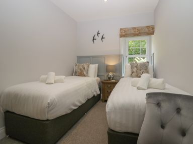 A bedroom with two single beds a bedside table lamp and a window with a blind at Garden Cottage No 1 in Keswick